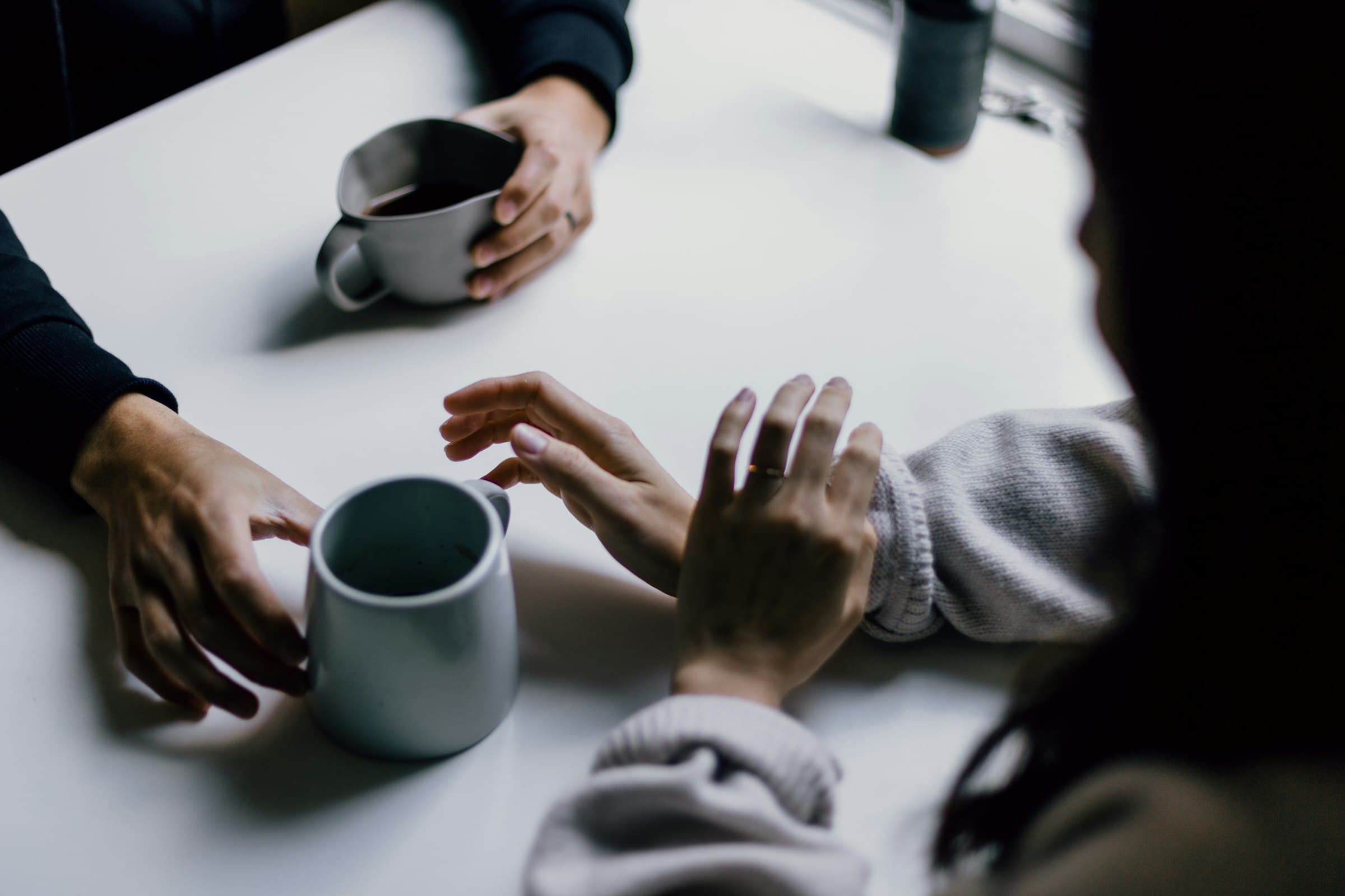 Two people talking across a white table, each with a cup of coffee.